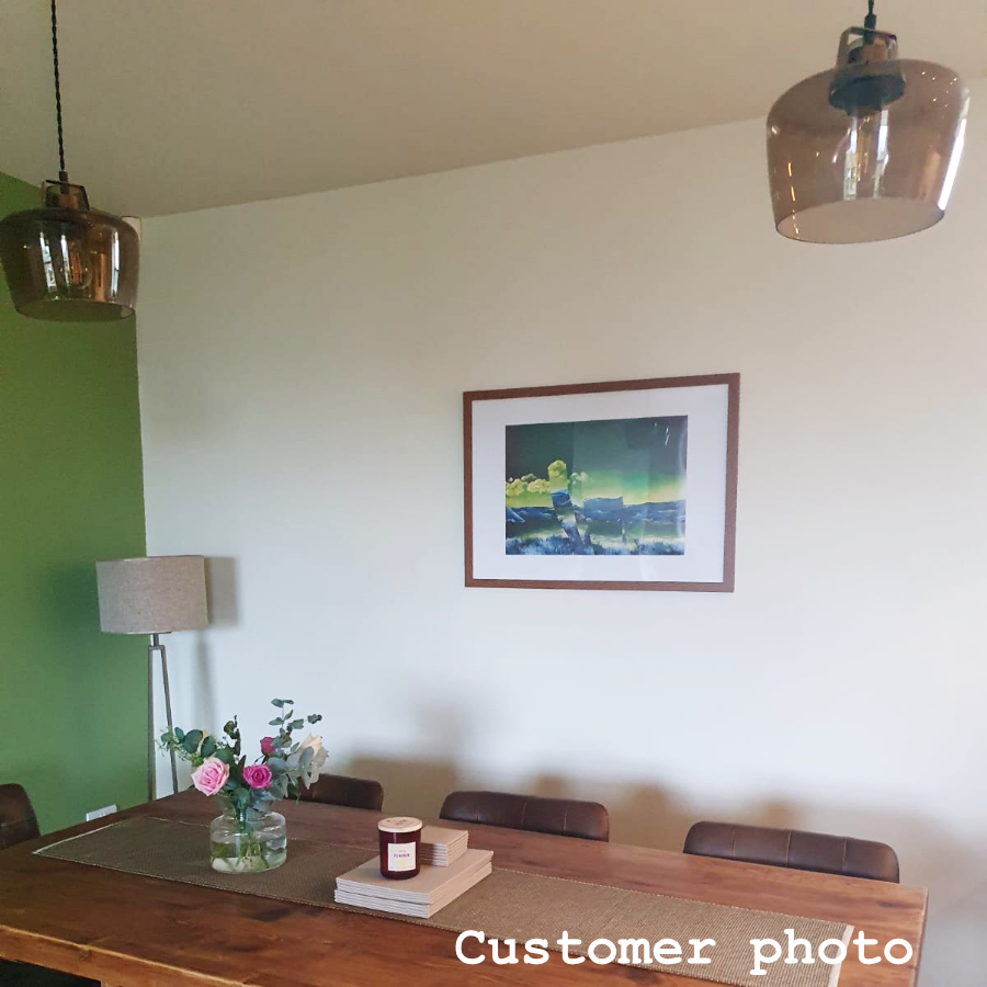 Customer photo of artist Rebecca Taylor's Opposite Landscape hanging in their kitchen, complemented by a white and green wall, a wooden dining set and wooden picture frame.