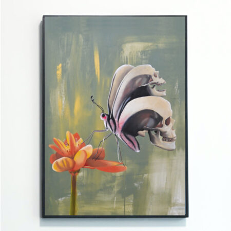 This Butterfly Skull print, by artist Rebecca Taylor, is mounted in a black frame against a white wall. It depicts a black and white butterfly whose wings contort into the shape of human skulls. The butterfly is resting on a yellow and orange flower against a green background.